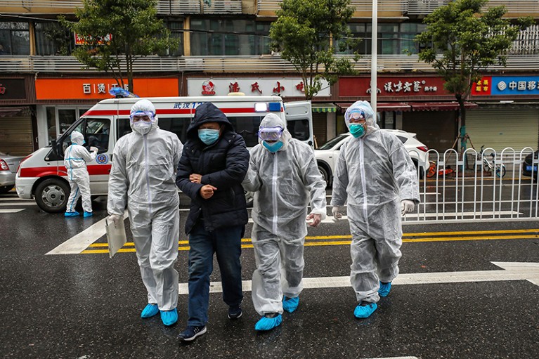 Medical workers in protective gear help a person to walk near an ambulance.