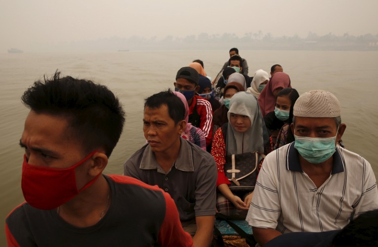Close-up of people packed into a small boat on a smoggy day, with some wearing face masks