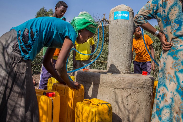 A young woman, among children and adults, fills jerrycans with clean water in Lode Lamhffo Kabele
