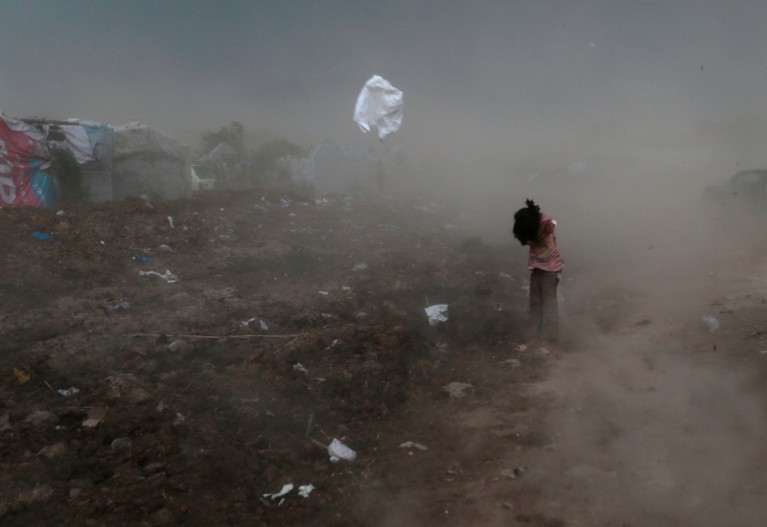 A young girl protects herself from garbage and dust raised by a gust of wind in a slum in Pakistan