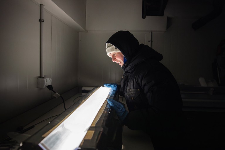 Rebecca Pyne, in a darkened cold room examining an ice core on a lightbox