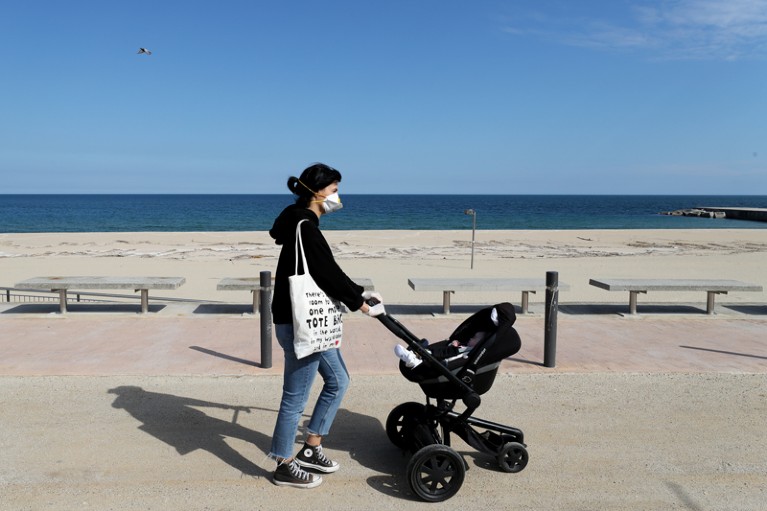 A woman wearing a face mask pushes a baby stroller while walking along the seafront