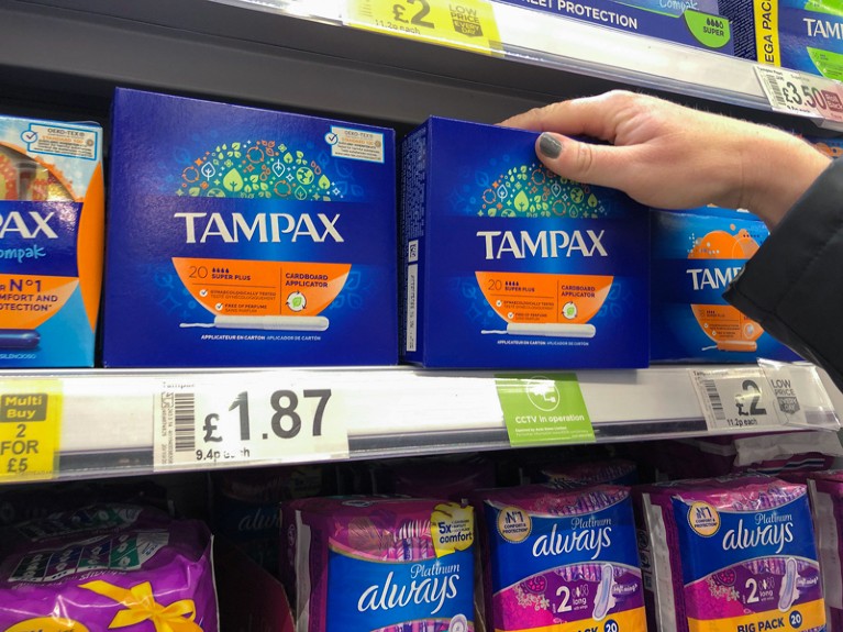 Close-up of a hand reaching for a pack of tampons in a supermarket