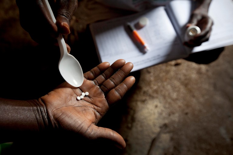 Close-up of a hand holding four small white circular tablets, using a plastic spoon for size comparison