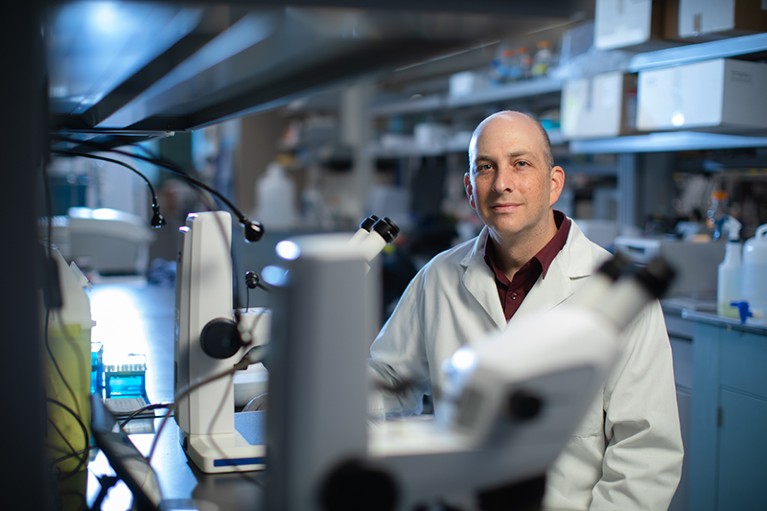 Jeremy Sivak sitting in a laboratory. A blurred microscope is seen in the foreground.