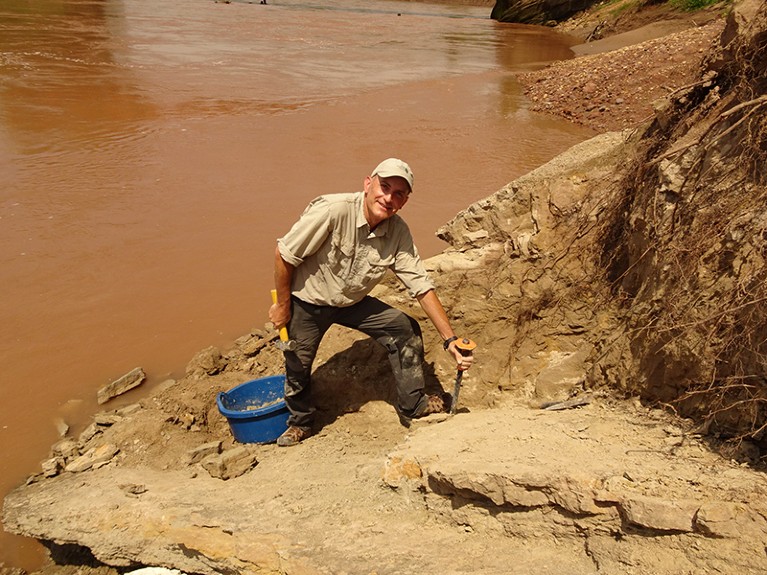 Laurent Marivaux standing on the banks of a river, holding a pick and a hammer