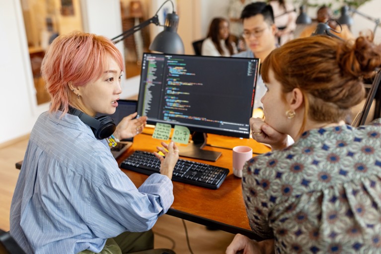 Female software developers discuss over the computer while sitting at a desk