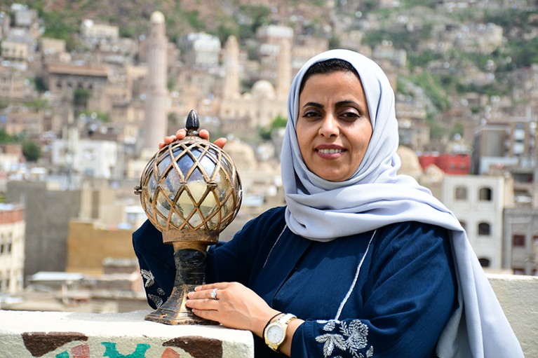 Portrait of Anjila Sultan, a mental health researcher in Yemen, with the Old City of Taiz in the background.