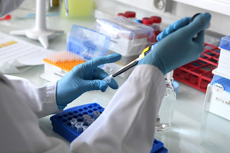 Close-up of gloved hands pipetting at a lab bench.