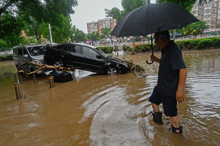 A man wades past a damaged car along a flooded street, after heavy rains in Mentougou district in Beijing.