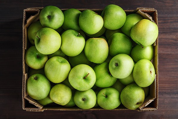 Green apples in a box on a wooden table.