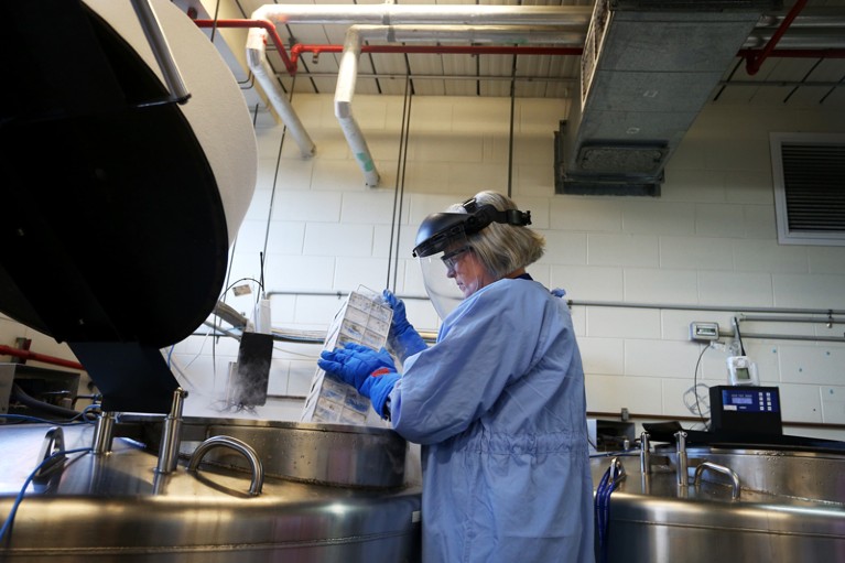 A Senior Hospital Scientist wearing full PPE extracts PBMC vials from tanks in a cryogenics facility