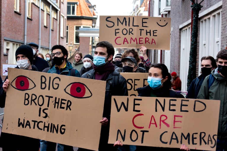 Students wearing face masks hold cardboard signs protesting the use of cameras at university