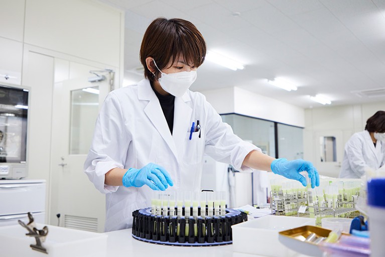 A researcher wearing gloves and a mask handles samples in a laboratory.
