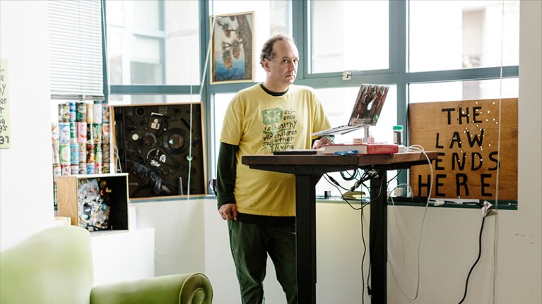 Michael Eisen, wearing a yellow top, at a standing desk.