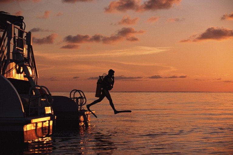 Silhouette of a diver stepping off a boat into the sea at sunset