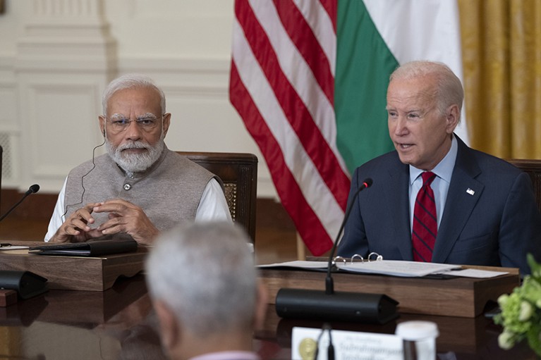 Narendra Modi and Joe Biden sit next to each other at a table, each with a microphone in front of them.