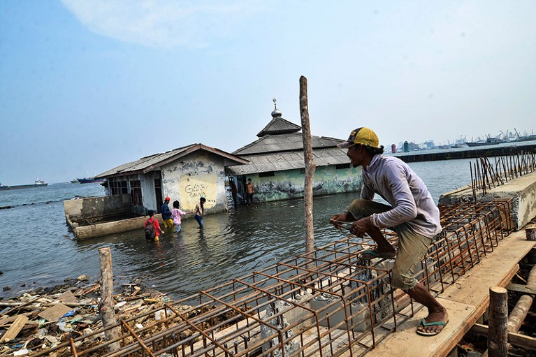 A man works on a seawall being rebuilt behind an abandoned mosque which has been surrounded by the sea.