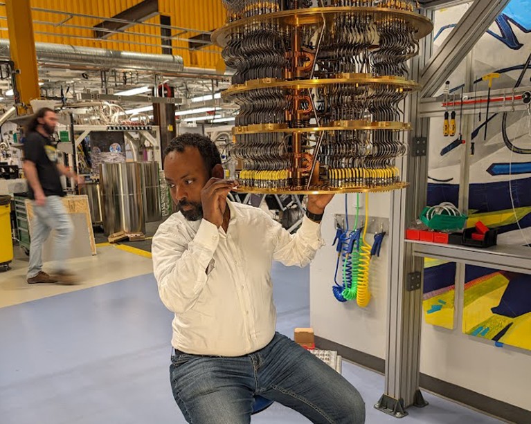 Abraham Asfaw sits on a chair and prepares a dilution refrigerator