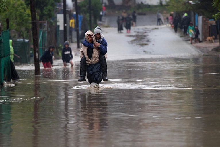A man carries an elderly man across a flooded road during heavy flooding in Sir Lowry's Village in South Africa.