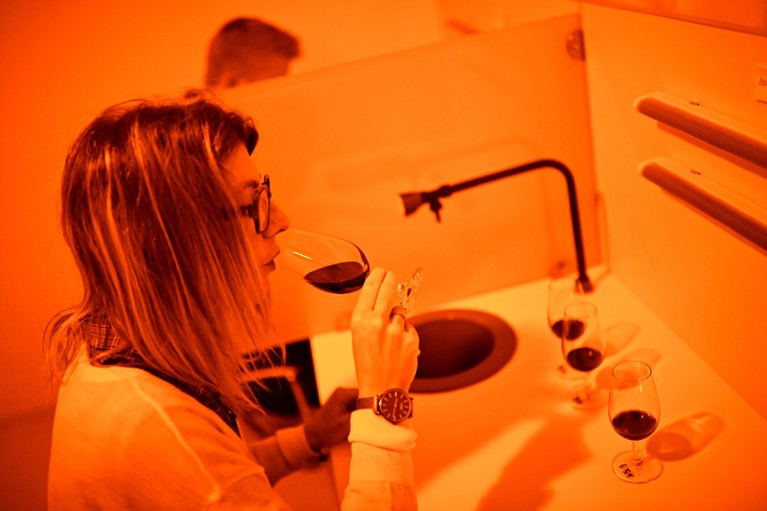 A woman samples a glass of wine in a room lit by orange lights