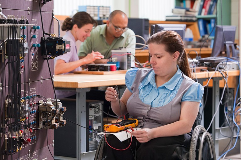 An engineering student in a wheelchair reading an ohmmeter while measuring contacts.