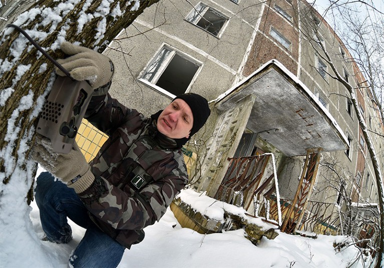 Denys Vyshnevskyi setting a photo-trap to a tree outside an abandoned block of flats in the ghost town Pripyat