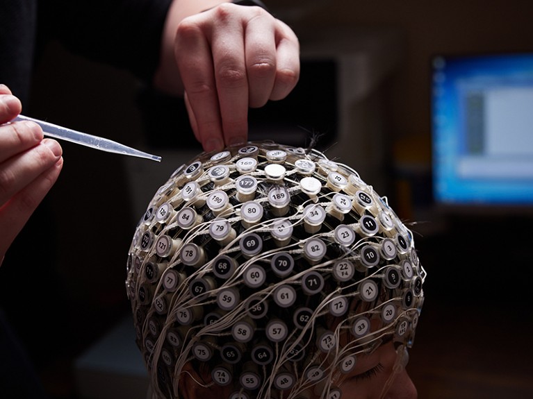 A person sits wearing a skull cap of electrodes for an electroencephalogram