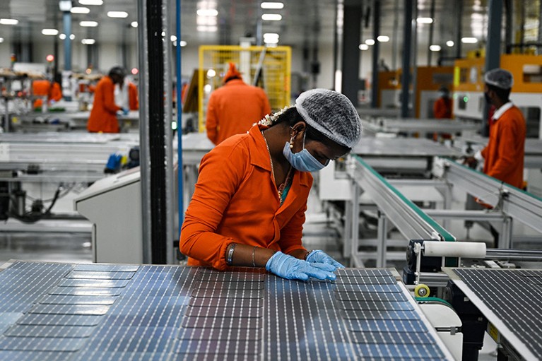 Person at centre of photo working on solar cells at a manufacturing plant. Other employees working in the background.