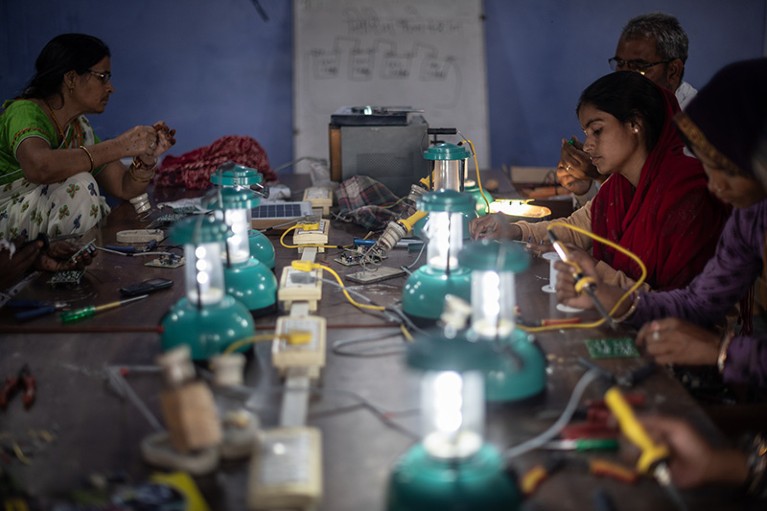 Several people are seated at a table, assembling solar lamps.