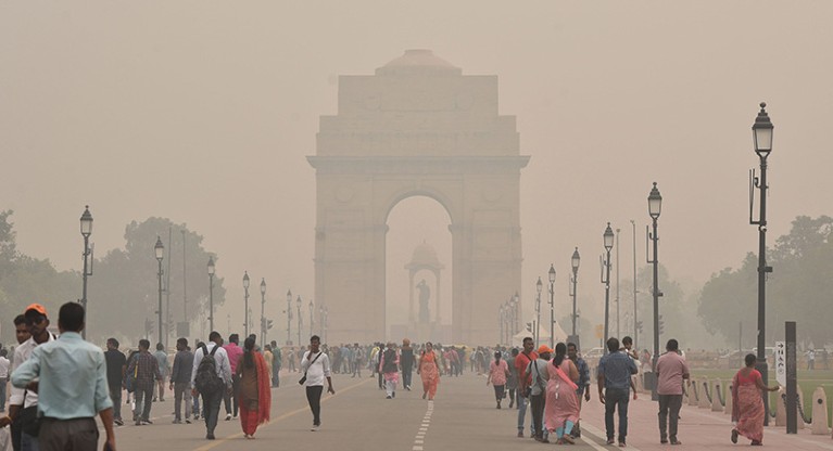 People walk along road engulfed by smog. A large archway in the background.
