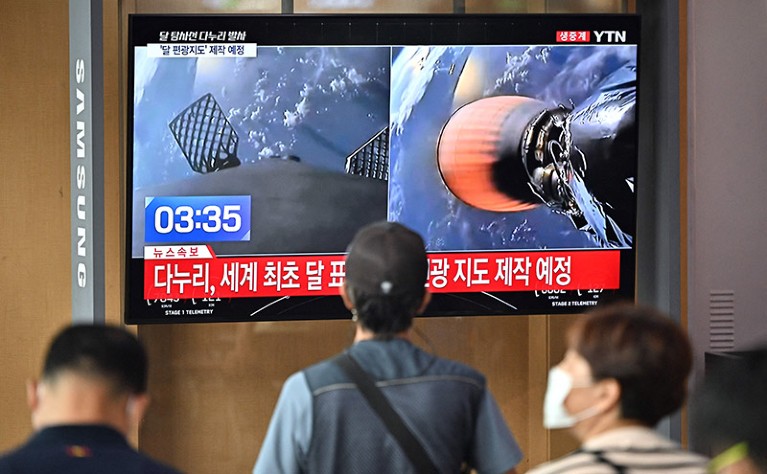 People watch a television screen showing a live footage of a SpaceX Falcon 9 rocket launching with South Korea's first lunar orbiter Danuri onboard.