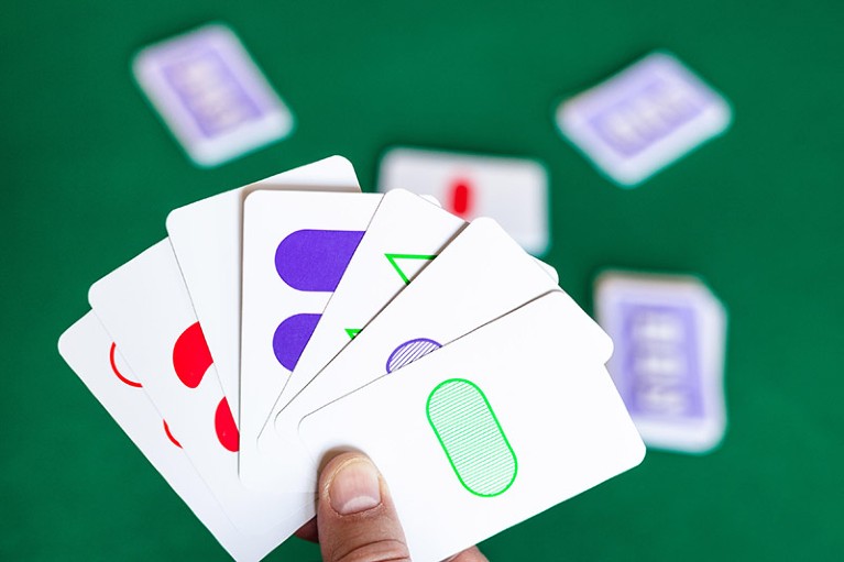 A player holds a hand of Set game cards over a green table.