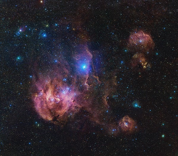 A wispy pastel pink nebula stretches across a sky studded with brightly shining stars.