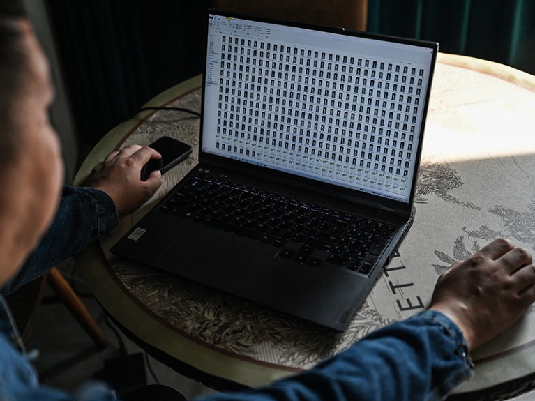A man works on a laptop whose screen is covered in rectangular icons.