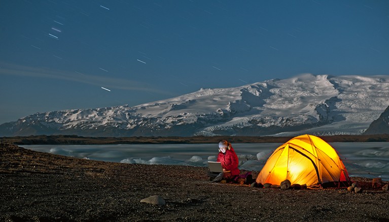 A scientist sits outside of her tent with laptop in the Arctic climate.