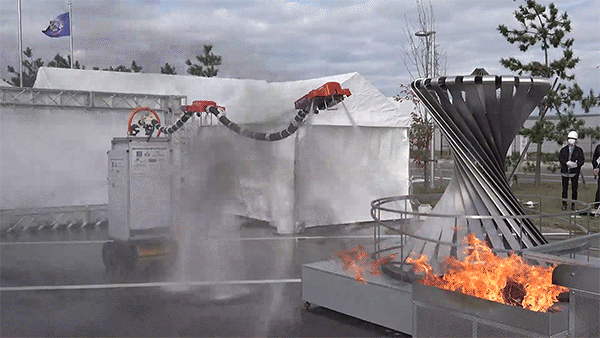 An animated gif showing a robot’s snake-like hose move towards a fire. The hose is held up by jets of water and connected to the robot’s main body, a large white box rolling along on sturdy wheels. When the robot hose reaches the fire, it extinguishes it with the water jets located in its ‘head’.