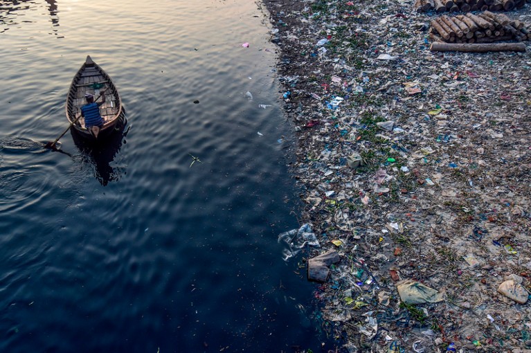 An aerial view of a man paddling on a boat as plastic bags float on the water surface of the Buriganga river in Dhaka