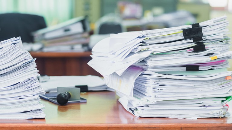 Piles of stacked paper documents pictured on an office desk.