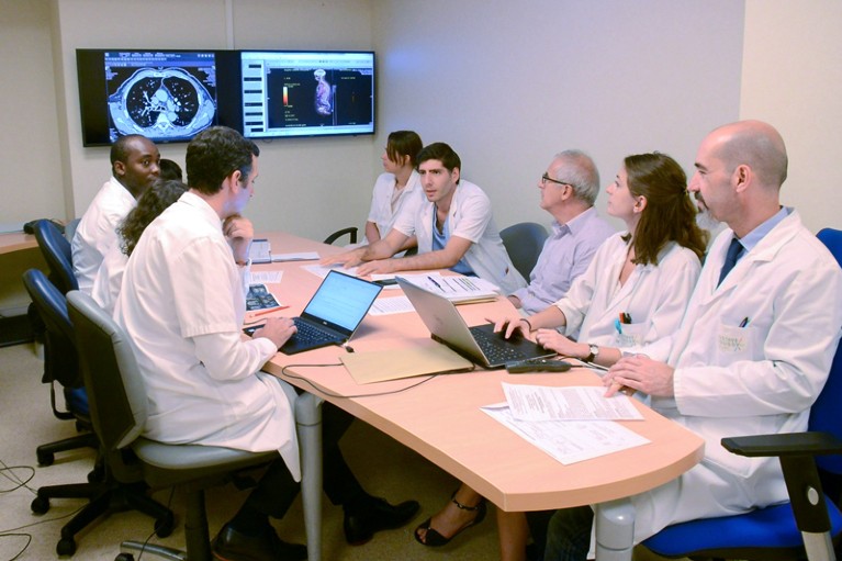 Un team clinico che indossa camici da laboratorio si siede attorno a un tavolo mentre discute dei pazienti