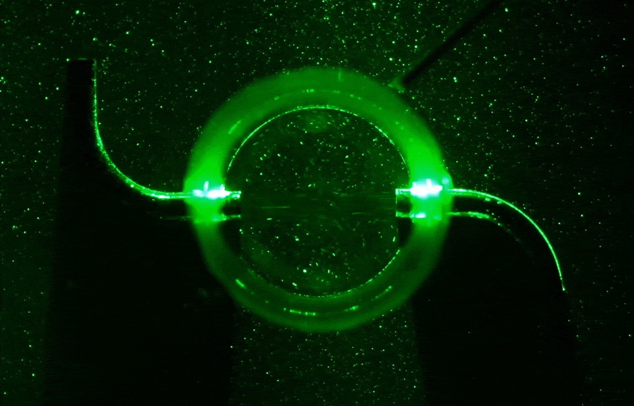 Video of an S-shaped sprinkler apparatus sucking in water, lit up green against a black background.