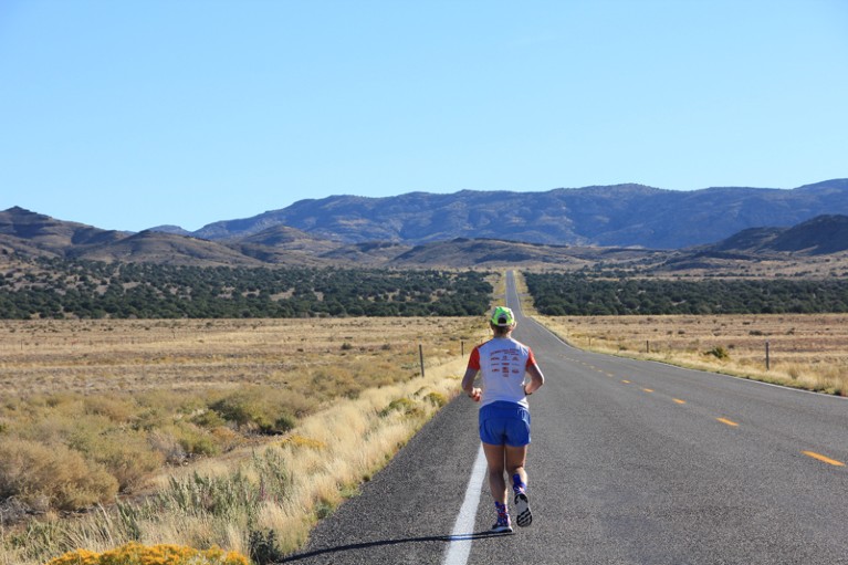 Rear view of Jenny running down a long straight road in Utah on a sunny day
