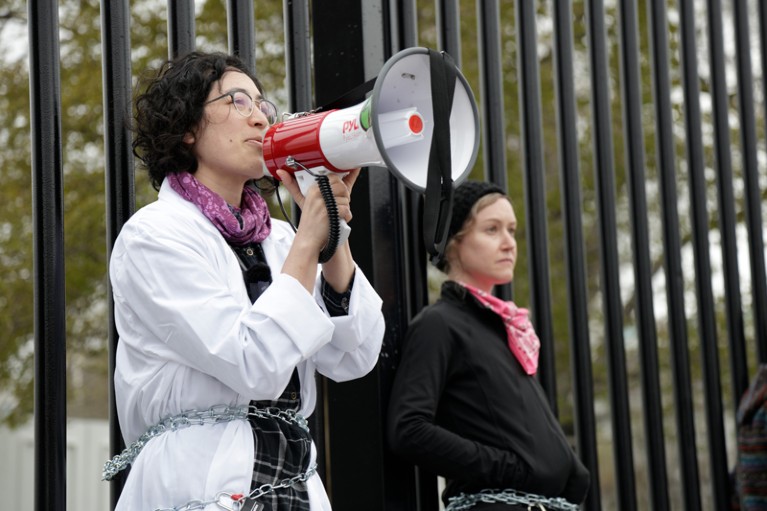 Rose Abramoff speaks into a megaphone while chained to a fence
