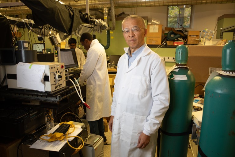 Gang Chen poses for a portrait in a white lab coat in the lab