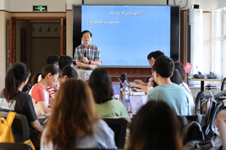 Yu Xie holds a microphone and gives a lecture to students on scientific publications