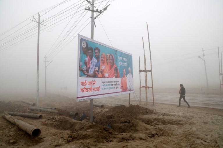 In very low visibility a person walks down a road past a billboard in support of Narendra Modi ahead of the 2024 general election