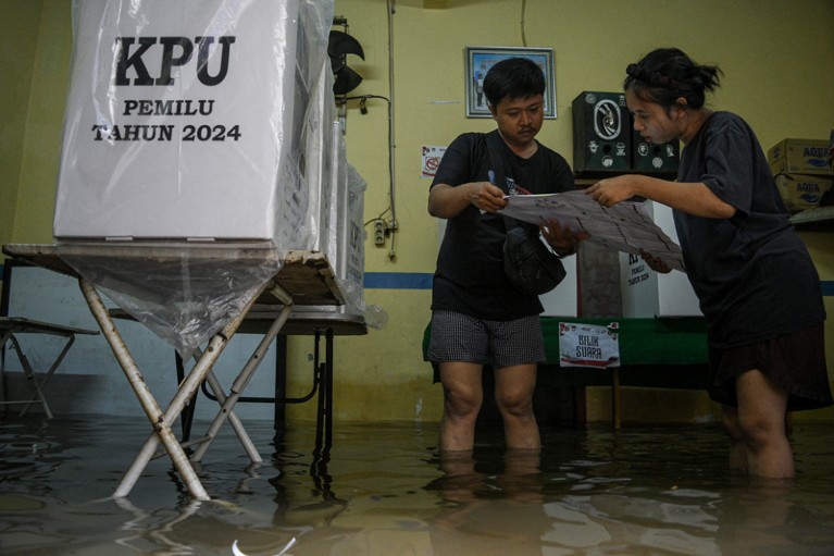 Electoral officers examine 2024 ballot papers at a flooded general election polling station in Indonesia
