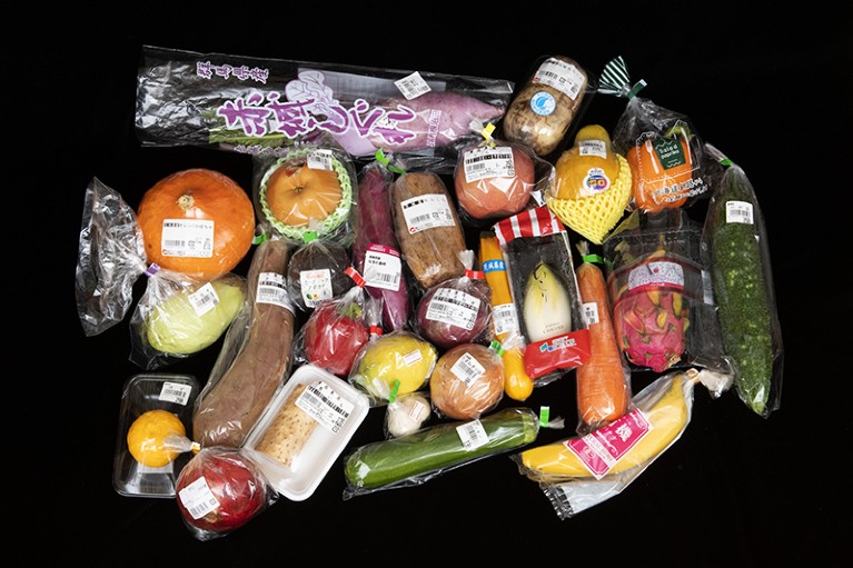 Individually plastic wrapped fruit and vegetables on a black background in Tokyo, Japan.