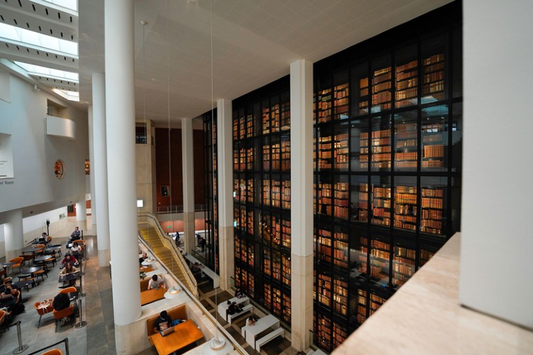 View of an atrium in the British Library with floor-to-ceiling book shelves and people reading as tables