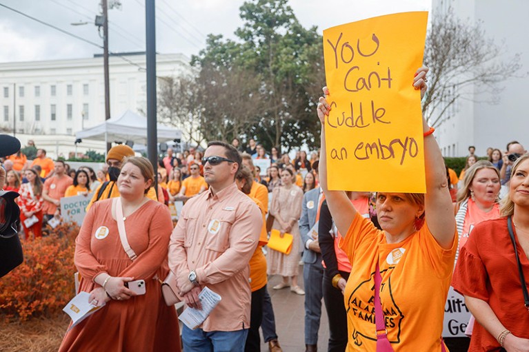 Surrounded by people dressed in orange, a woman holds a sign as part of a rally advocating for IVF rights outside the Alabama State House.